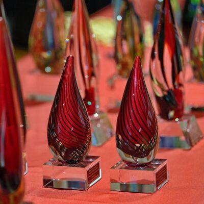 Glass figures shaped like a teardrop on top of a square glass base, red with black lines swirling down in parallel