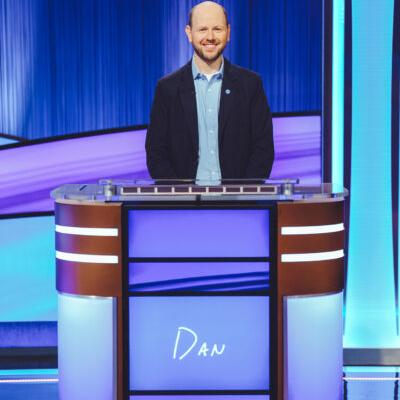 Dan Moren, mostly bald with a beard and a smile, standing at the Jeopardy podium with the word "Dan" on it