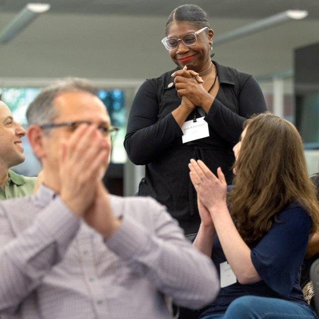 		People in an audience applaud one person standing
	