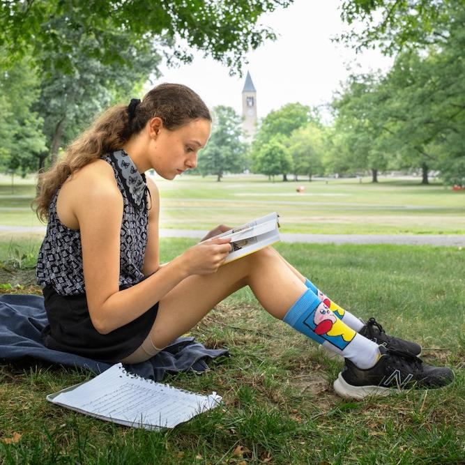 		Person sitting on grass, reading a book propped on knees
	