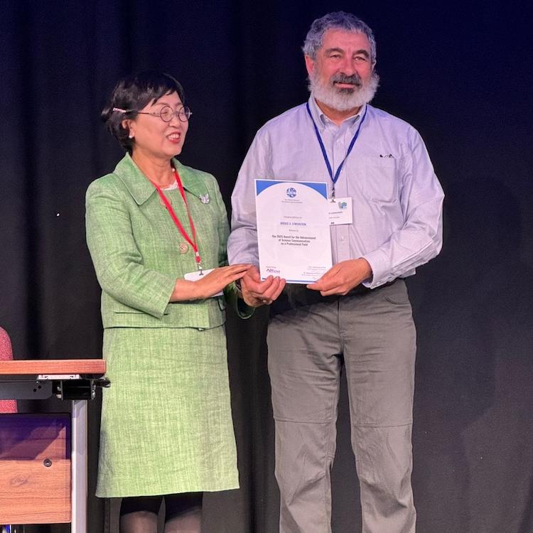 		Two people standing on a stage, holding a certificate between them
	