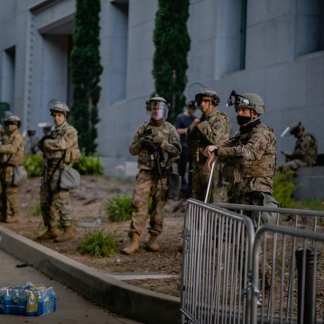 		people in military fatigues stand by the side of a street
	
