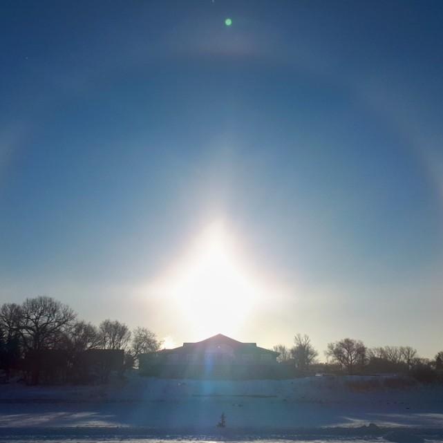 		In the sky, a perfect half circle appears around a rising sun with two bright "sun dogs" on either side
	