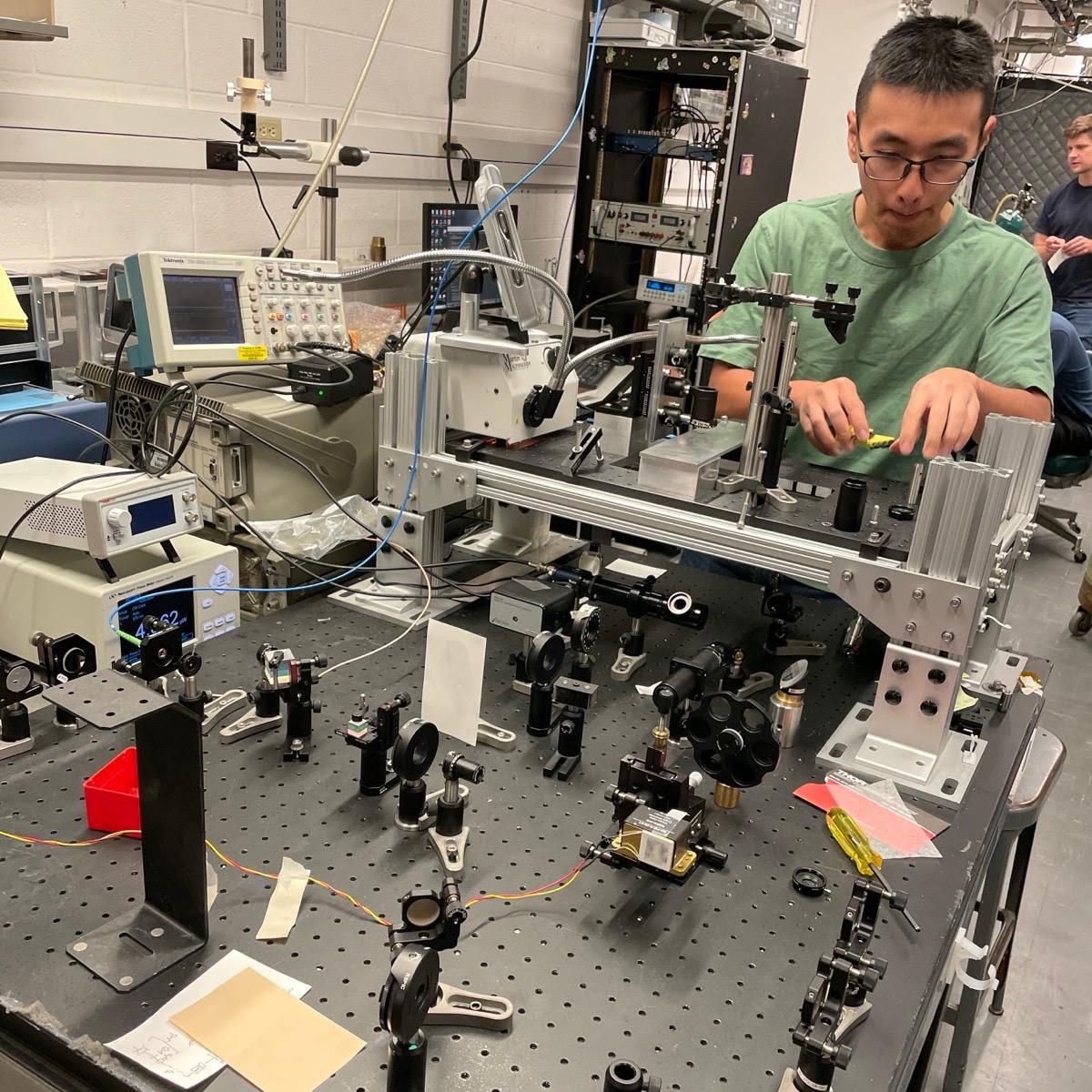 		Man with glasses and t-shirt working on complex electronic table-top machine
	