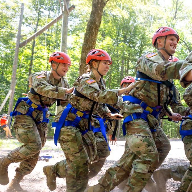 		Several people in Army fatigues and red helmets run, strapped together
	