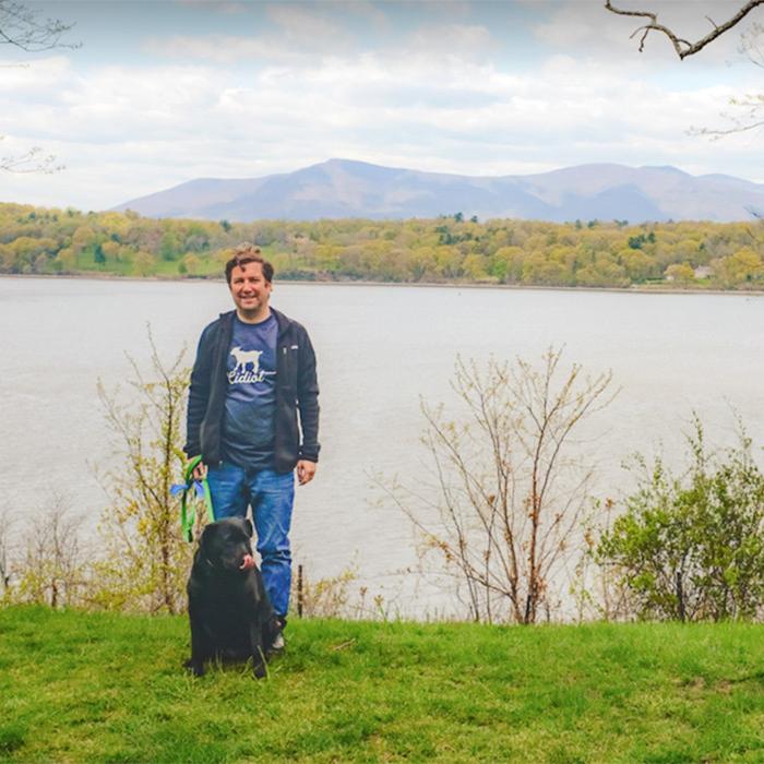 Person standing with a dog on the bank of a river