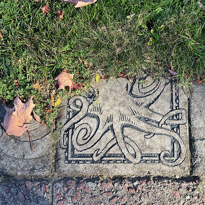 Close up of a paving stone carved with an octopus, next to grass