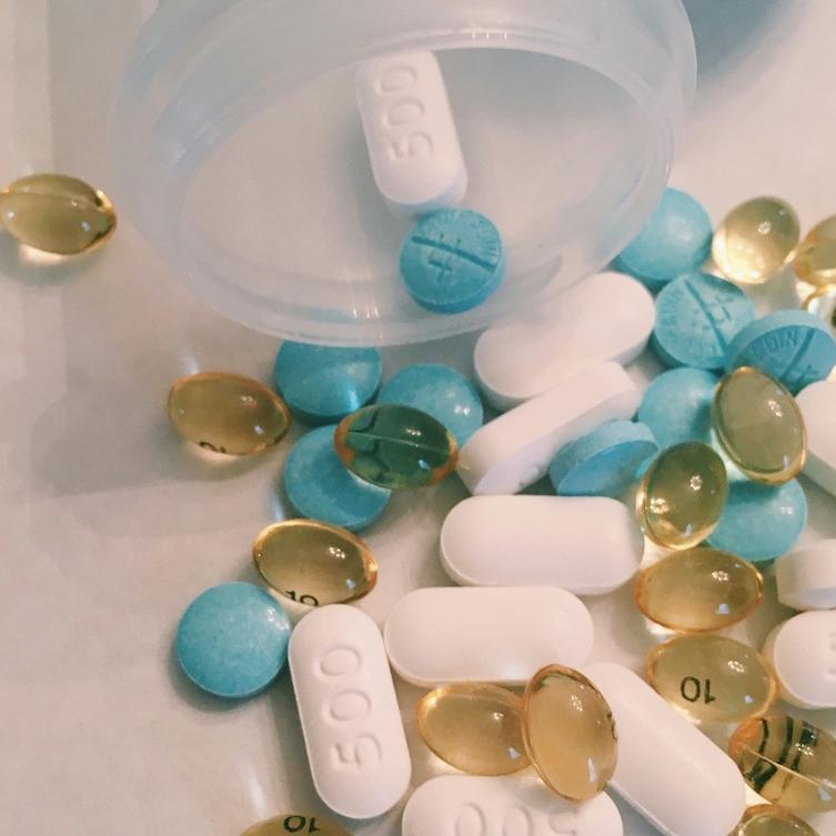 close-up of pillls of sevreal sizes and colors, spilling out of a bottle