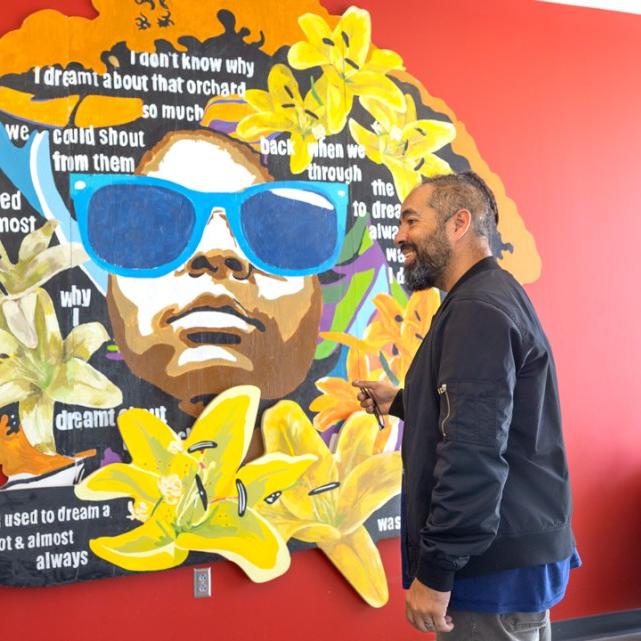 Two people stand with a colorful mural between them