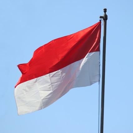 Flag with broad red stripe on top and broad white tripe on bottom on flagpole against a blue sky.
