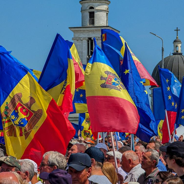 		Blue sky, stone spire with a cross on top, people holding red, yellow and blue flags
	