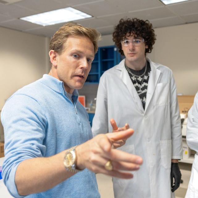 		three people; two in lab coats, looking at the third, who is pointing instructively
	