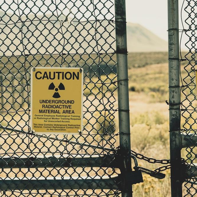 Chain link fence with yellow warning signs: CAUTION, UNDERGROUND RADIOACTIVE MATERIAL AREA