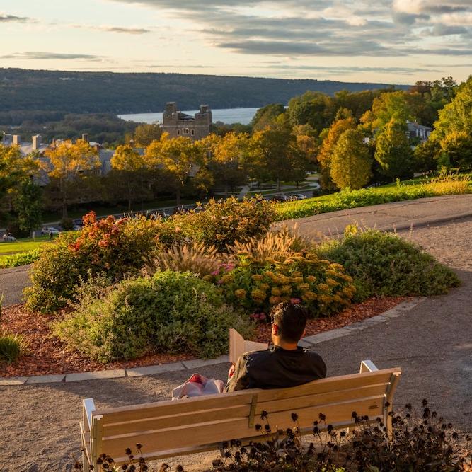 		People reading on benches that overlook a grand view of a lake and autumnal trees
	