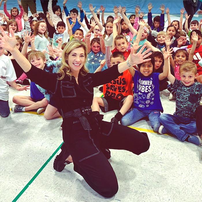 		Person in black jump suit poses in front of a crowd of excited children
	