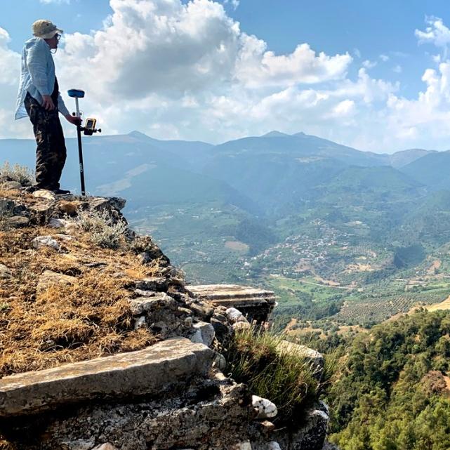 Person standing on a rocky hill, looking out over a huge, green plain