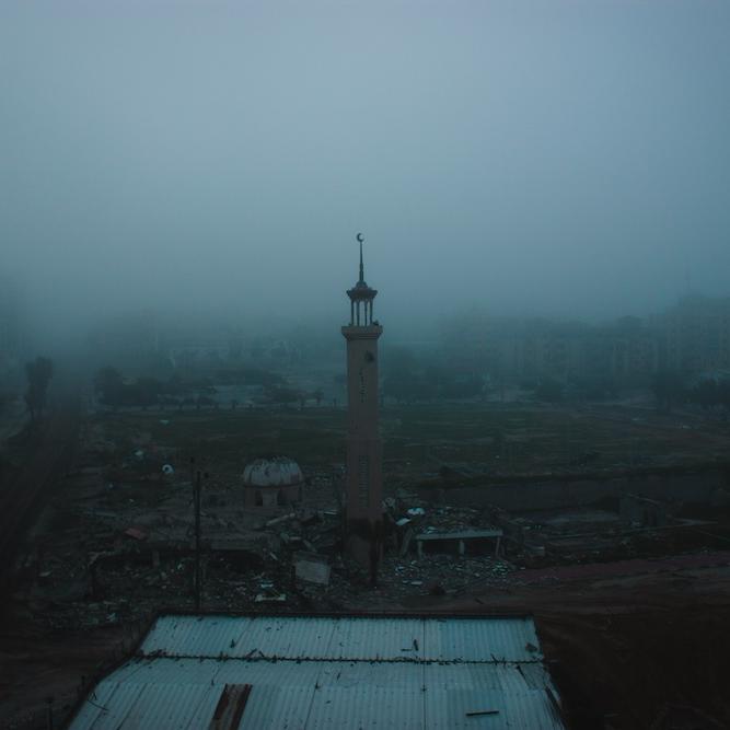 mosque spire rises in fog over a war-damaged street