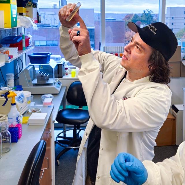		Two people work in a lab, looking up a a tube
	