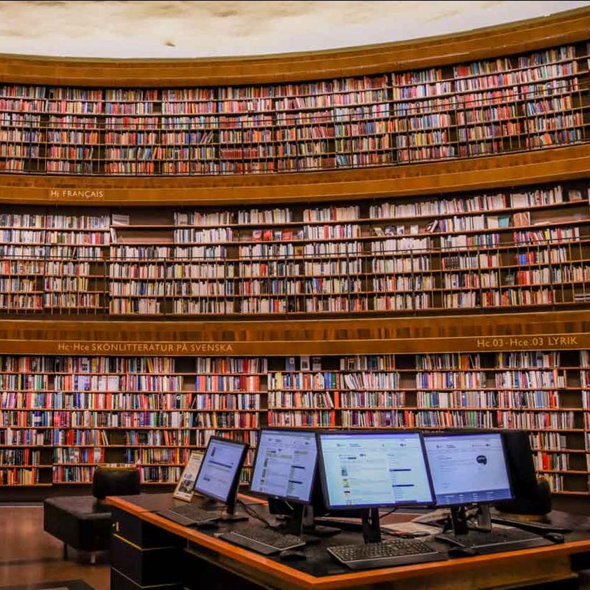 		books in a library with computers on table
	