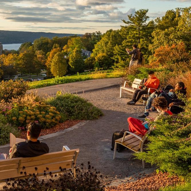 		People sitting on benches, reading with a lake and forest vista in front of them
	