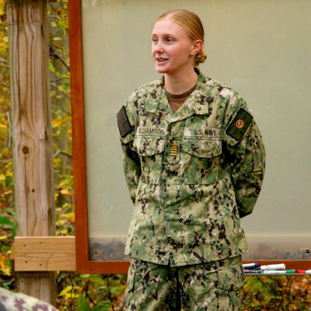 Person in military fatigues standing in front of others, speaking