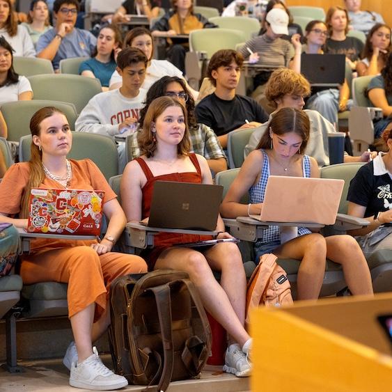 		Dozens of college students sit at attention in an auditorium with tiered seating
	