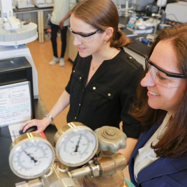 		Two people wearing lab safety glasses read a computer screen
	