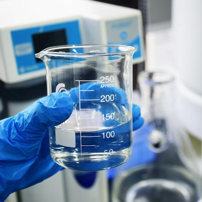 hand in a blue glove holding a beaker with clear liquid in it