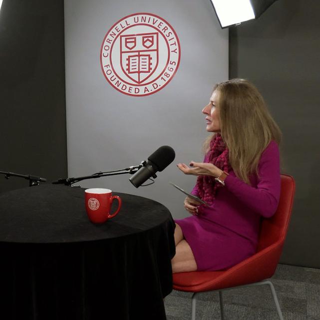 		Two people conversing at a black round table, talking into microphones
	