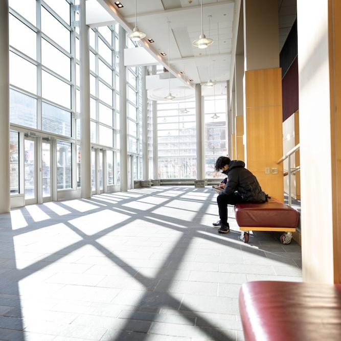 person reading on a bench in a large, sunny, modern room