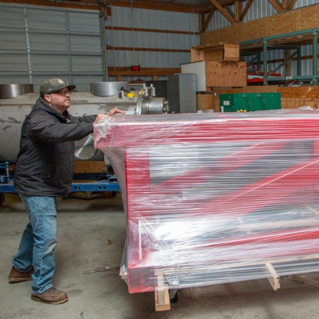Person pushing, on a dolly, a large red frame wrapped in plastic