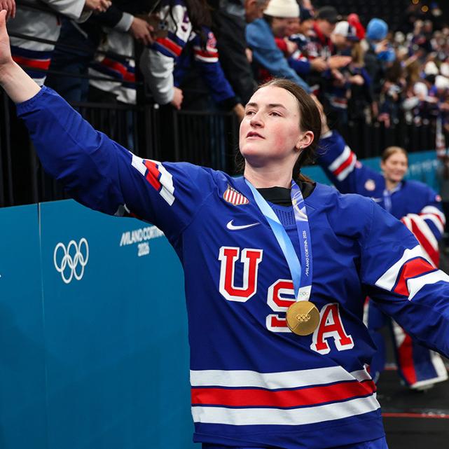 		Person in a blue USA jersey reaches up to slap hands with a member of the crowd, celebrating
	