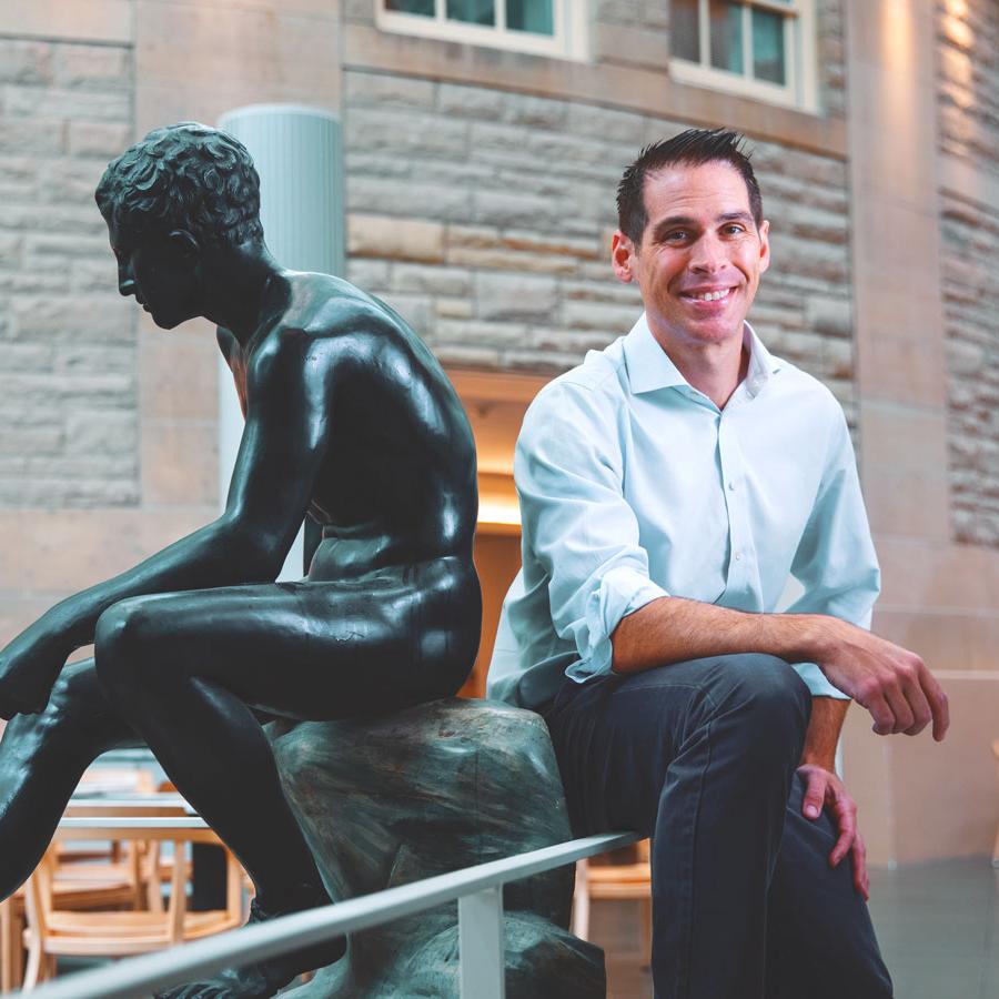 Person smiling next to a sculpture of a person sitting