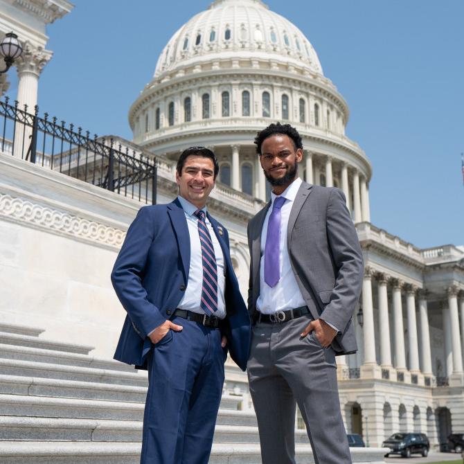 		Two people in suits standing in front of the recognizable white dome of the US Capitol Building
	
