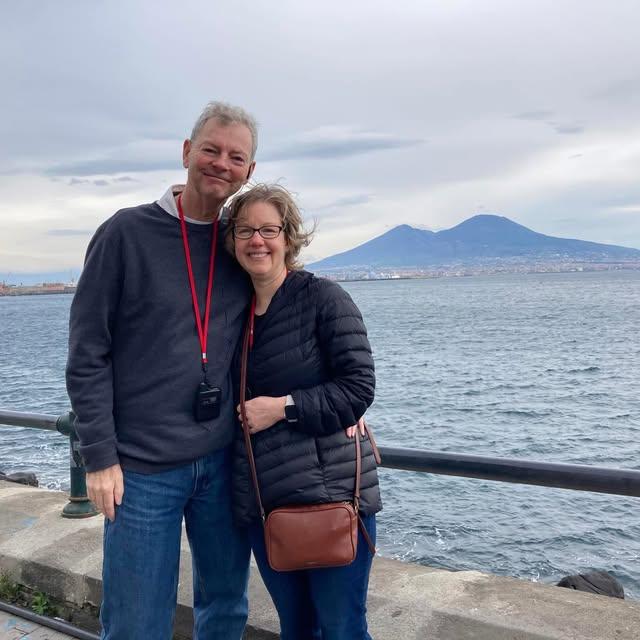 Robert Sullivan and wife Susan standing together on the deck of a sailboat out at sea.