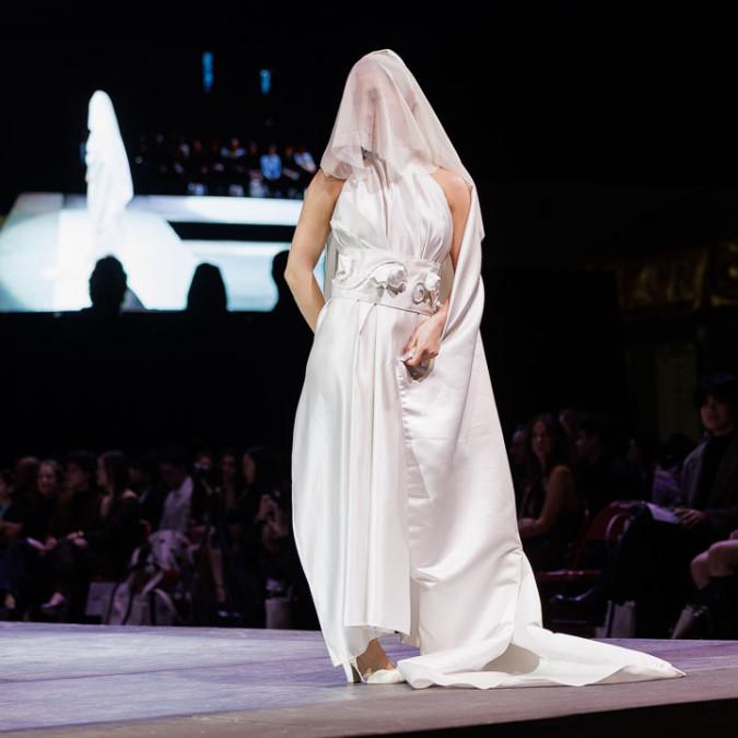		A person walking down a runway wearing a white dress
	
