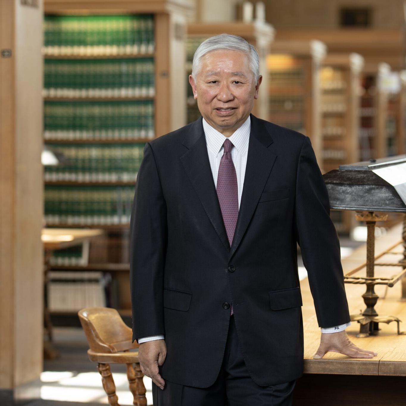 Person wearing a business suit stands in a law library with rows of book stacks behind him