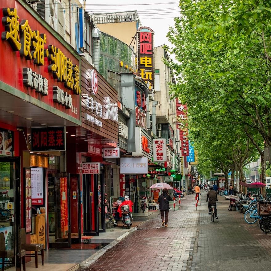 		City street with people on a walkway and bright signs in Chinese lettering
	