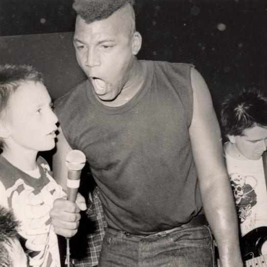 Black and white photo of a person hollering into a microphone with an intense look on his face