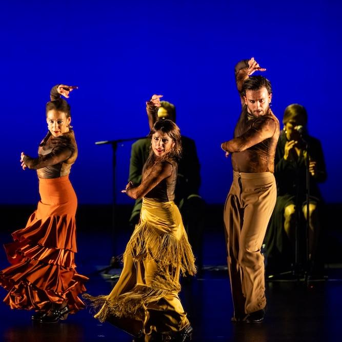 People on a stage, dancing dramatically in yellow and orange costumes