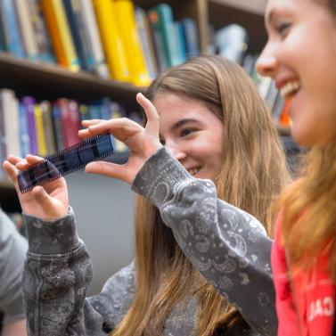 		High school students smiling and looking at an old photo negative.
	