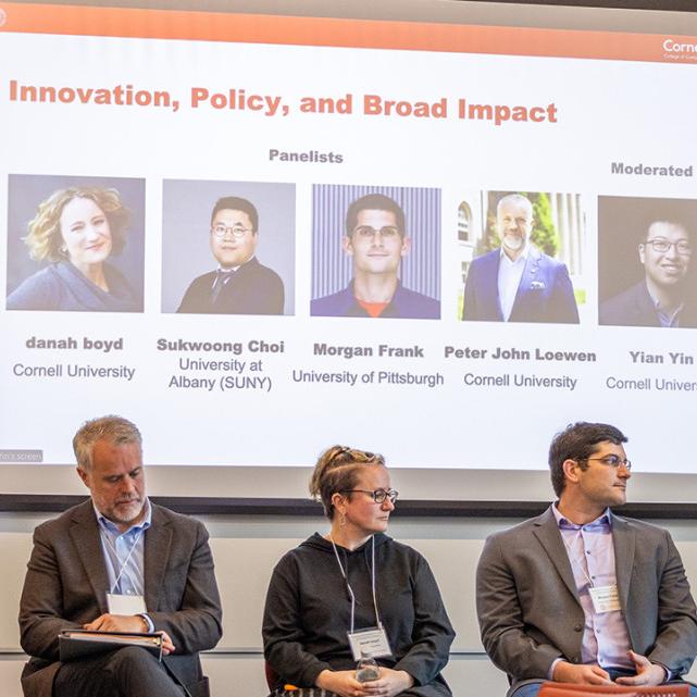 Five people on a stage with a screen behind them