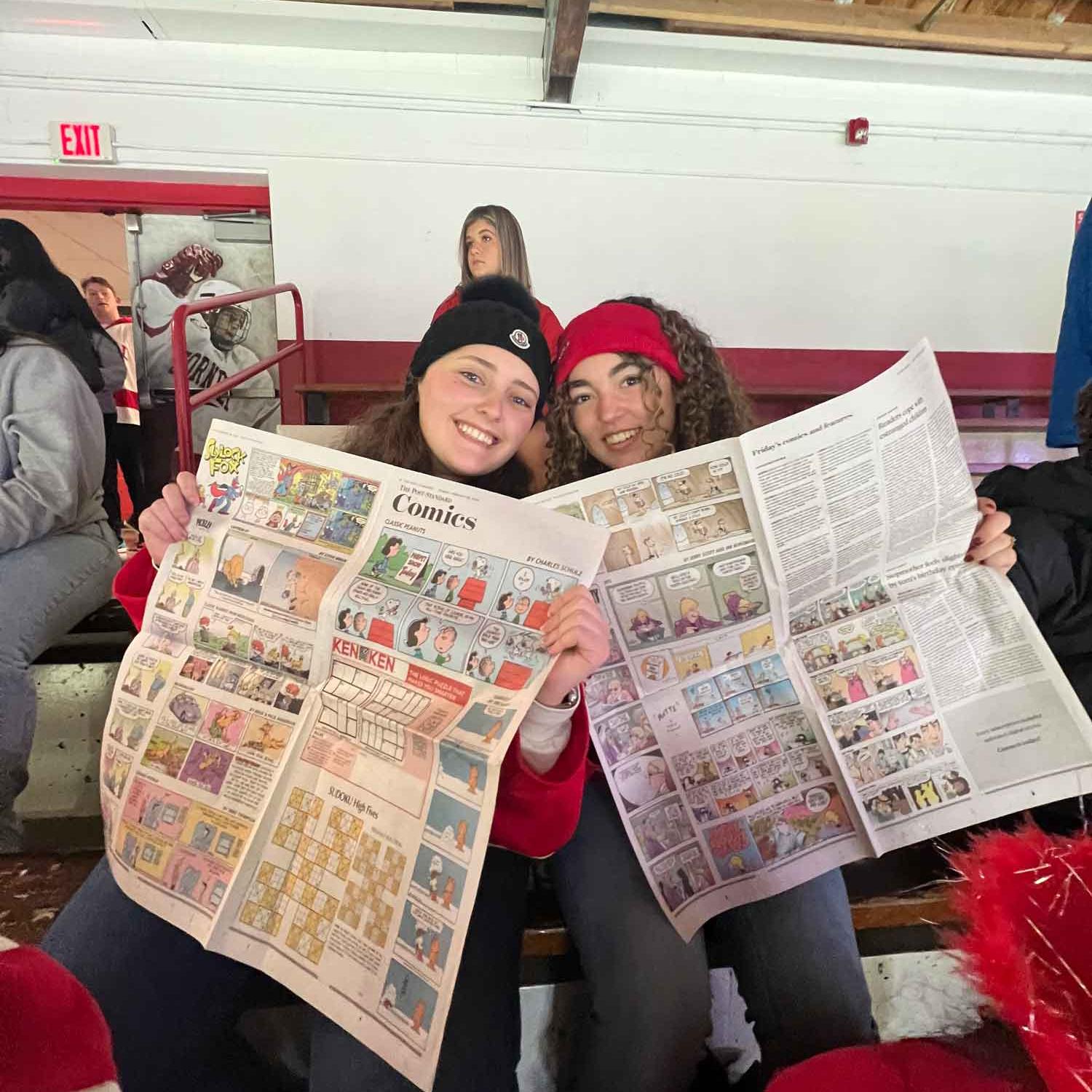 two people holding newspaper at a hockey game