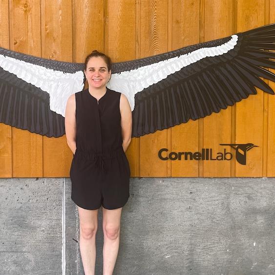 		Person in a black outfit standing so a very large pair of black and white wings – a lifesize model of a California condor – spreads out behind her. It looks like she has wings
	