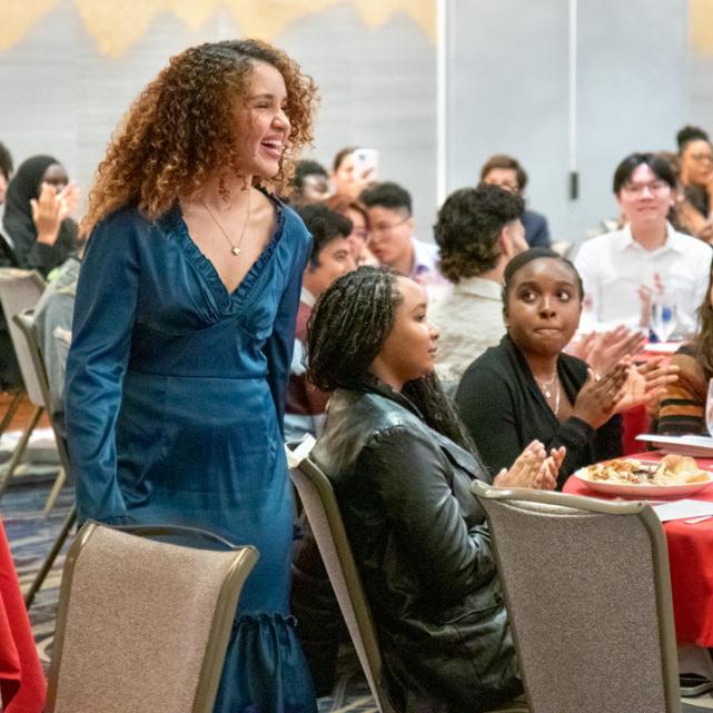 Person walking past a table where others sit, looking on and applauding