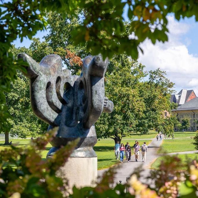 an abstract sculpture in the foreground with a grassy college quadrangle in the distance, bordered by low buildings