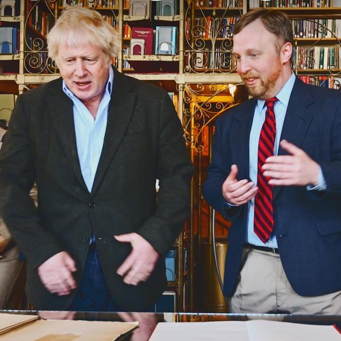 Two people discuss papers laid out on a table while a third looks on from the left