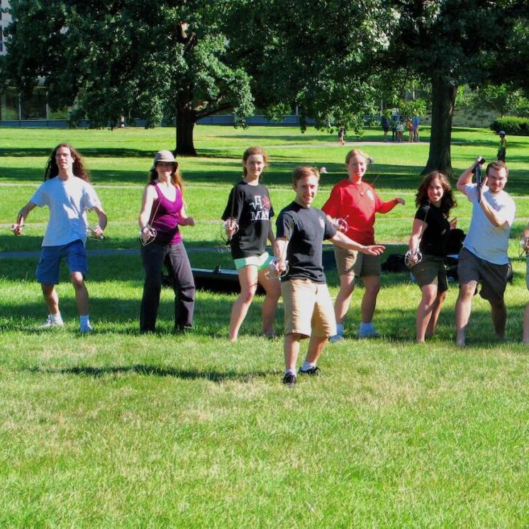 Several people pose imposingly with swords on the green lawn of Cornell's Arts Quad