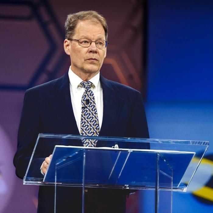 Person standing at a podium, looking serious