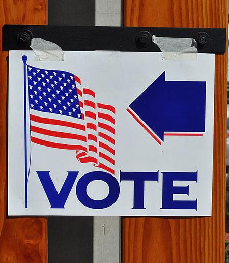 		 election poster taped to a wall with a picture of an American flag and an arrow pointing to the word &quot;vote&quot;
	